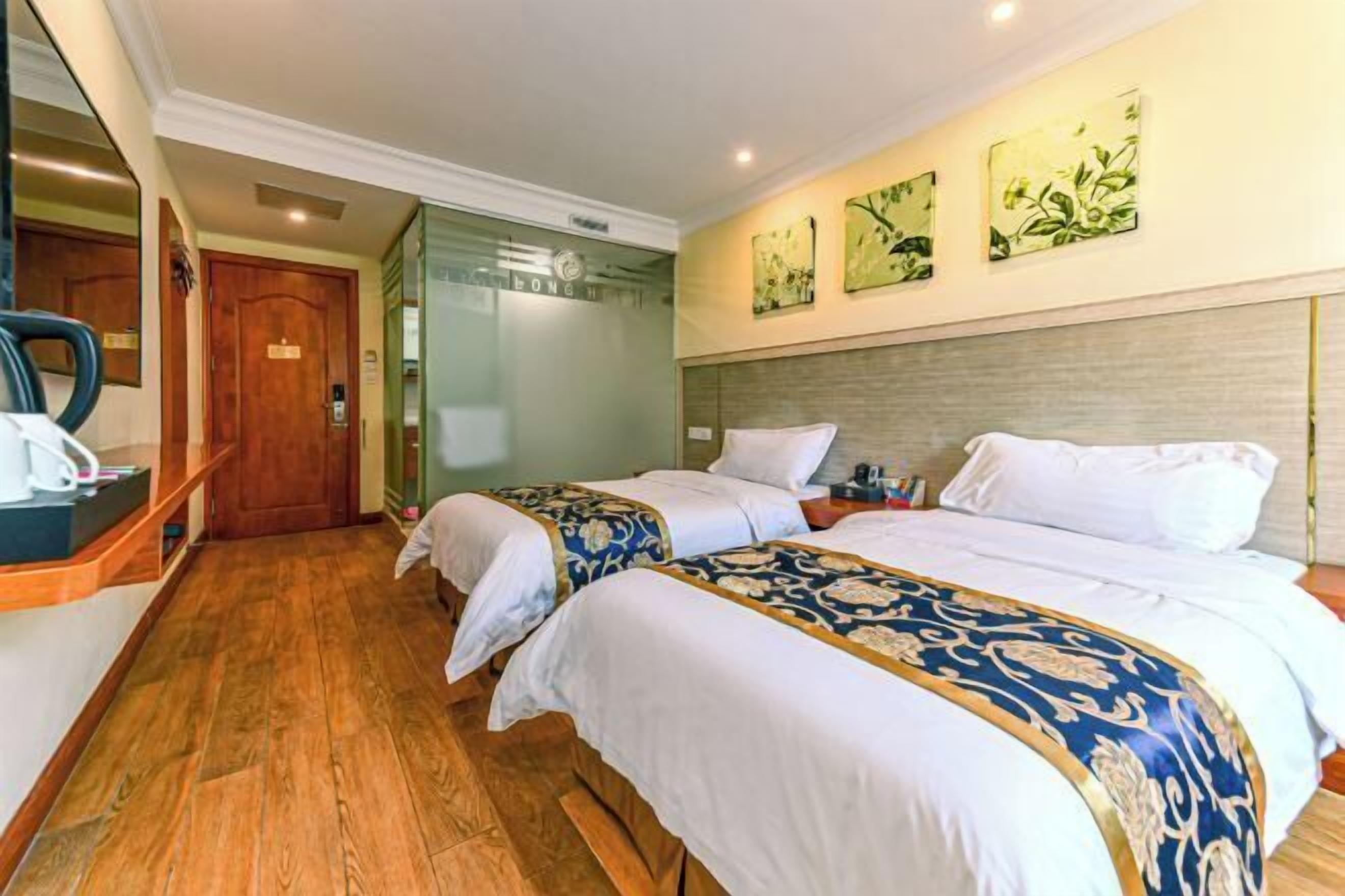 A hotel room with two beds, wooden flooring, a mirror, and artwork on the wall.