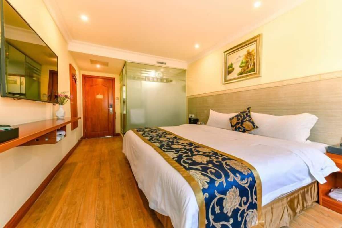 Una habitación de hotel con cama, mesita de noche, espejo, puerta y un cuadro colgado en la pared.