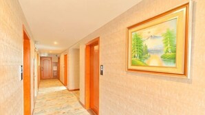 Un pasillo de hotel con puertas de madera, una alfombra estampada y un cuadro con paisaje en la pared.