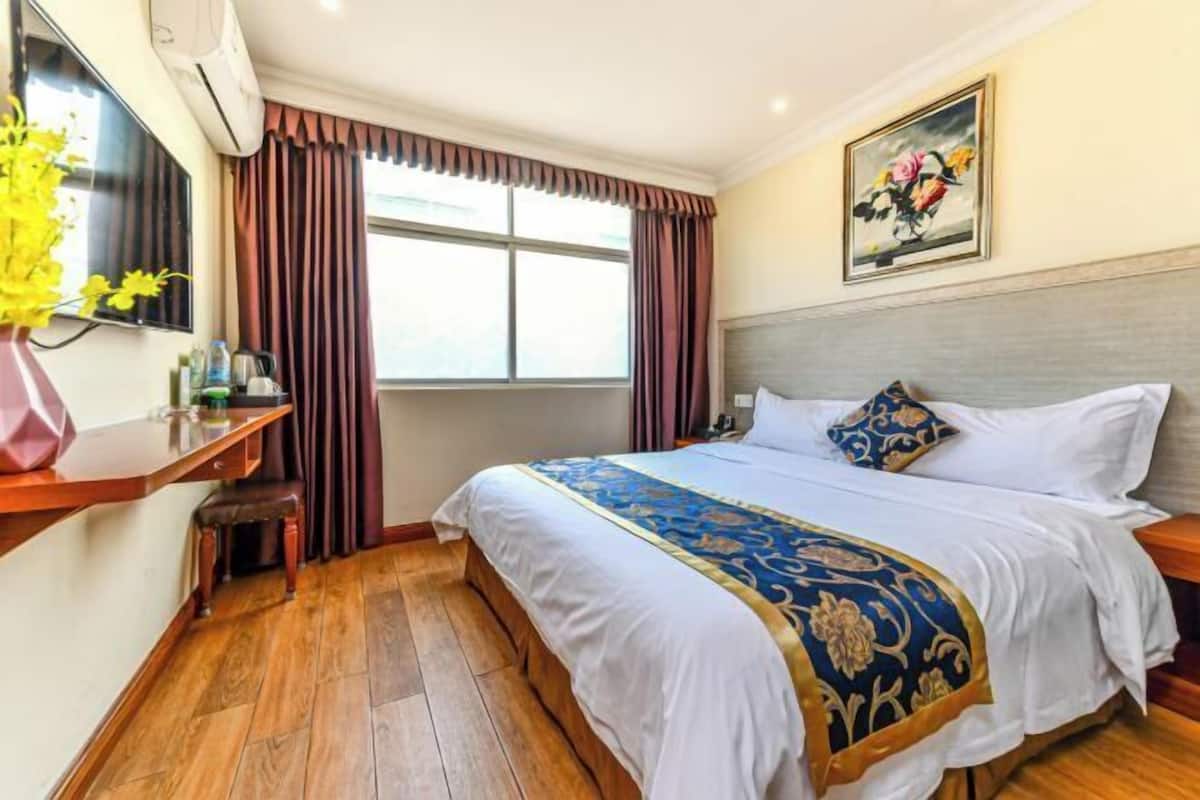 Habitación de hotel con cama, escritorio, silla, ventana con cortinas y un cuadro en la pared.