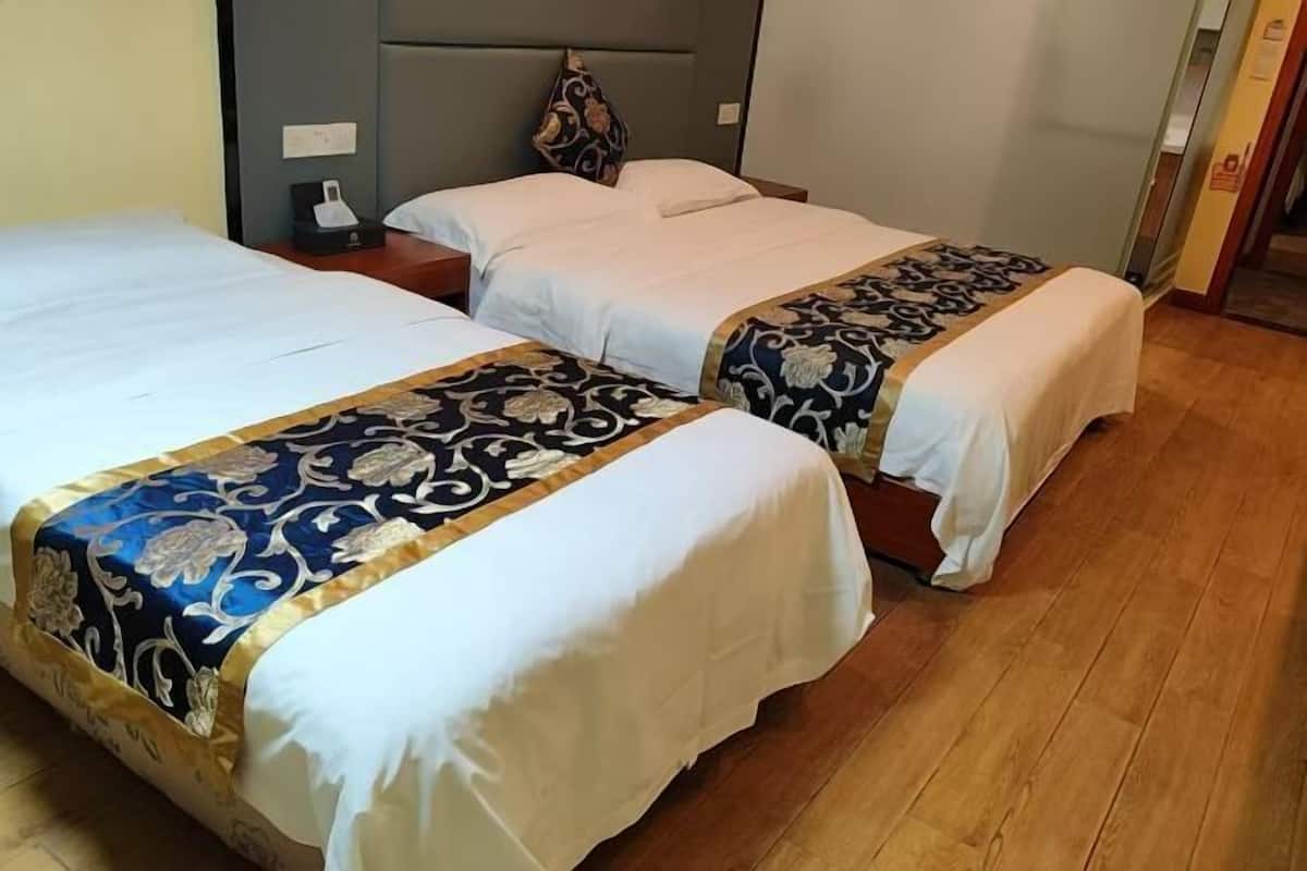 Dos camas individuales con ropa blanca y cabeceros decorativos, una mesita de noche con lámpara, y suelo de madera.