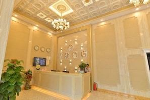 A hotel reception area with a reception desk, a chandelier, a television, and a wall-mounted clock.