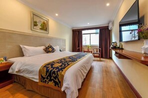 A hotel room with a large bed, a wooden headboard, a flat-screen TV, a desk with a chair, and a window with curtains. - Zhuhai Xilong Apartment (Zhuhai)