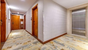 Un pasillo de hotel con puertas de madera, piso estampado y un ascensor.