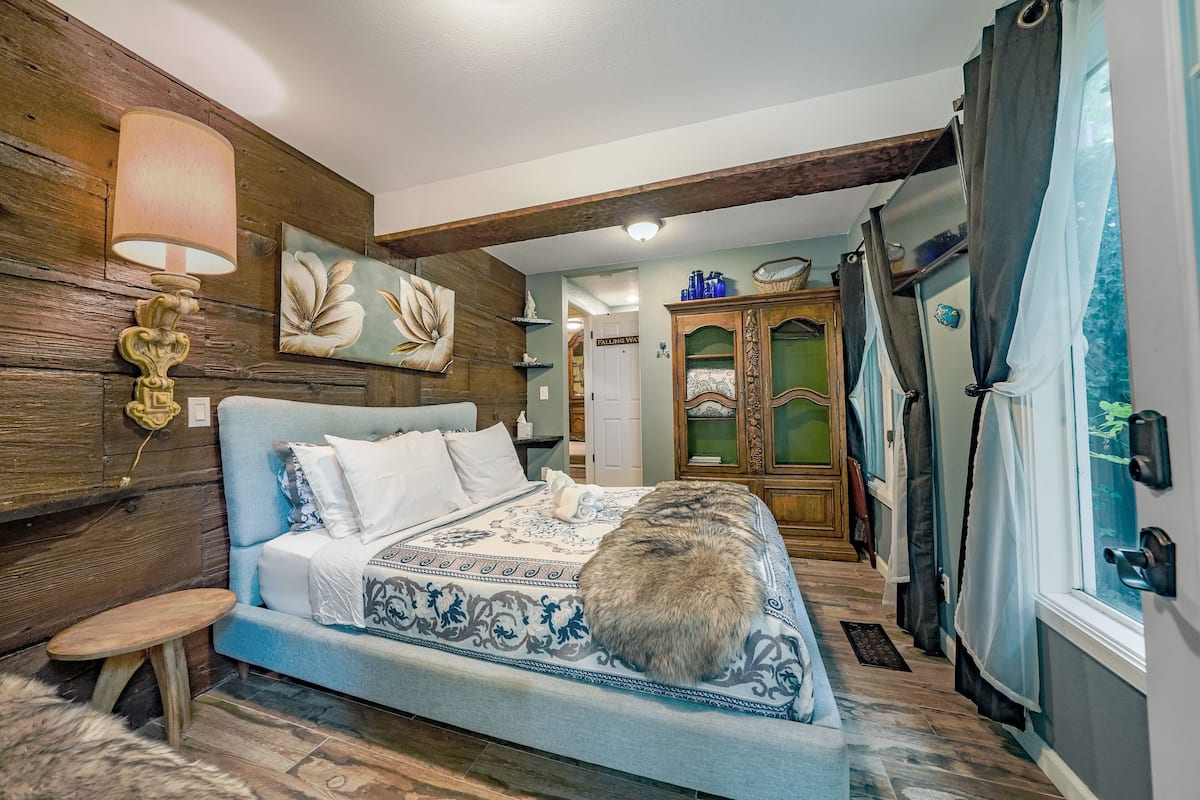 A bedroom with a large bed, wooden walls, a small table, and a cat on the bed.