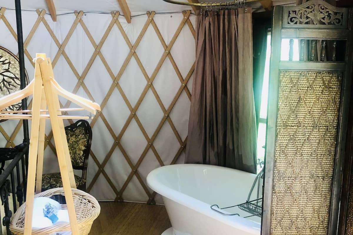 A cozy room with a large bathtub, a wooden ladder, a wicker basket, and a patterned door.
