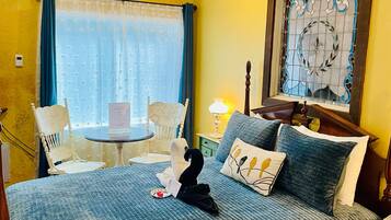 A hotel room with a bed, a chair, a small table, and a window with curtains.