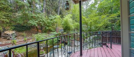 A wooden deck with a metal railing overlooking a garden with a pond and various plants.