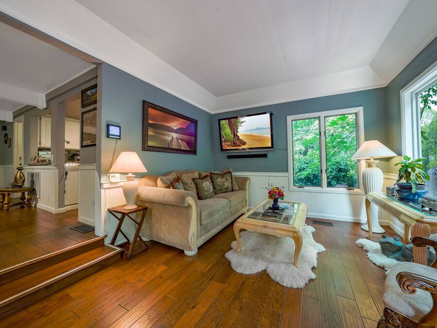 A living room with hardwood flooring, a beige sofa, a glass coffee table, and a view of the outdoors through a large window.
