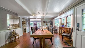 A spacious dining area with a large wooden table, surrounded by chairs, in a well-lit room with hardwood floors and large windows. - Flume's End (Nevada City)