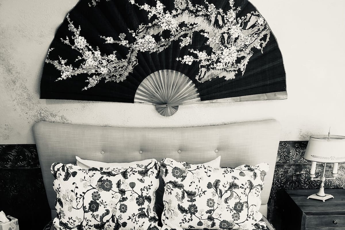 A bed with floral bedding, a fan, and a bedside table with a lamp.