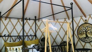Una cama con dosel y cortinas, una cesta de mimbre y un adorno en la pared en una habitación con techo a tienda.