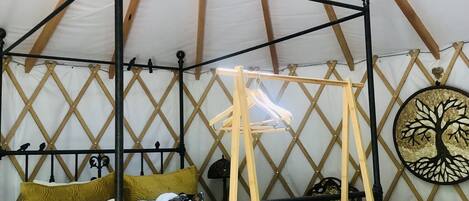 Una cama con dosel y cortinas, una cesta de mimbre y un adorno en la pared en una habitación con techo a tienda.