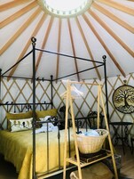 Una cama con dosel y cortinas, una cesta de mimbre y un adorno en la pared en una habitación con techo a tienda.