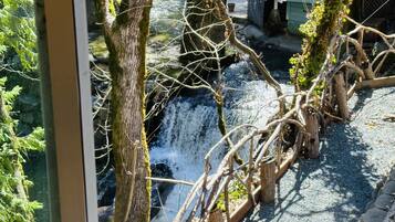 A view of a stone bridge over a small waterfall, surrounded by trees and greenery.