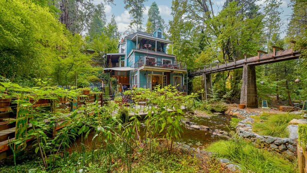 A two-story house with a wooden deck and a stone bridge over a stream. - Flume's End (Nevada City)