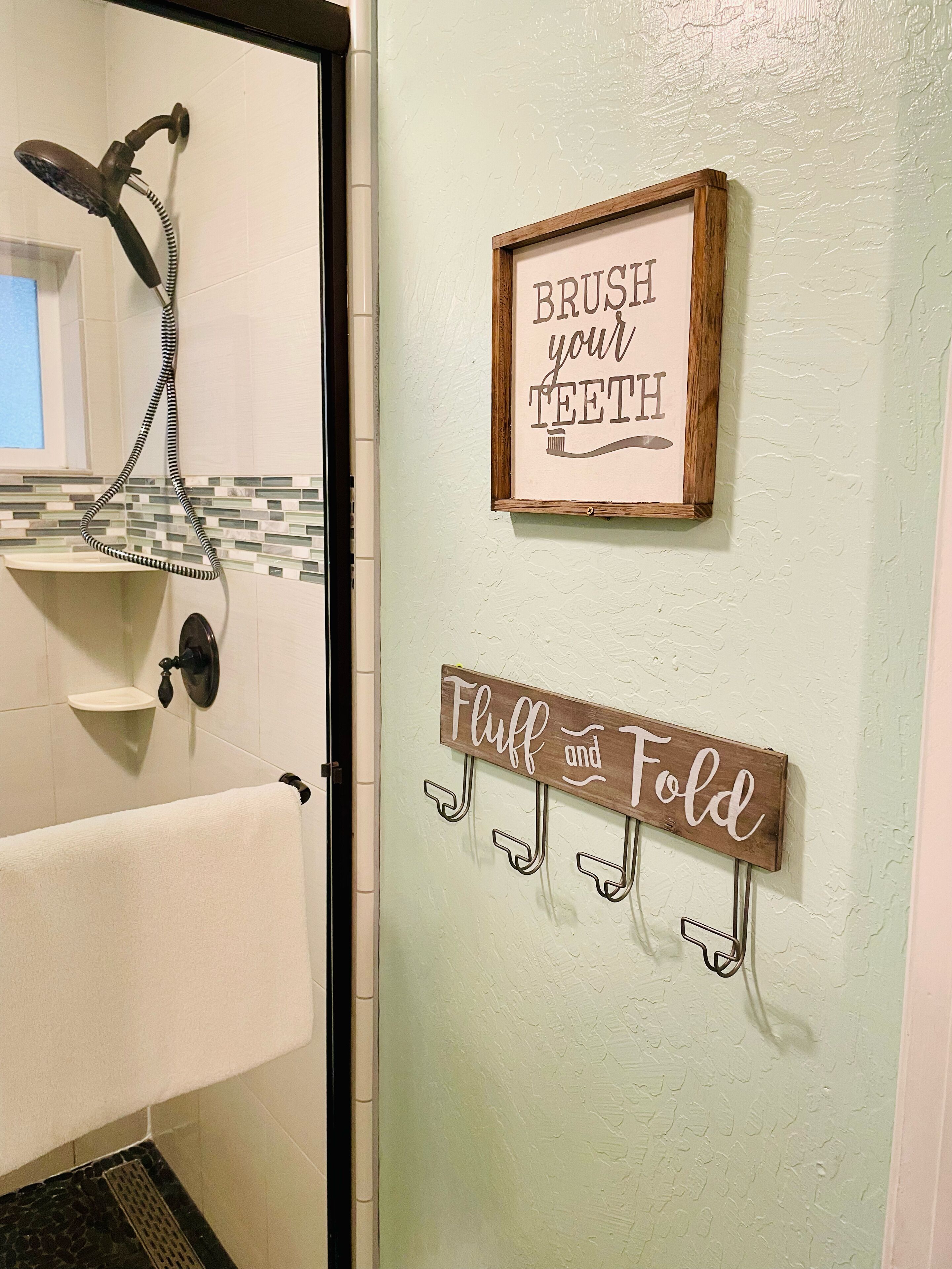 Une salle de bain avec une douche, un porte-serviettes et deux panneaux affichés sur le mur.
