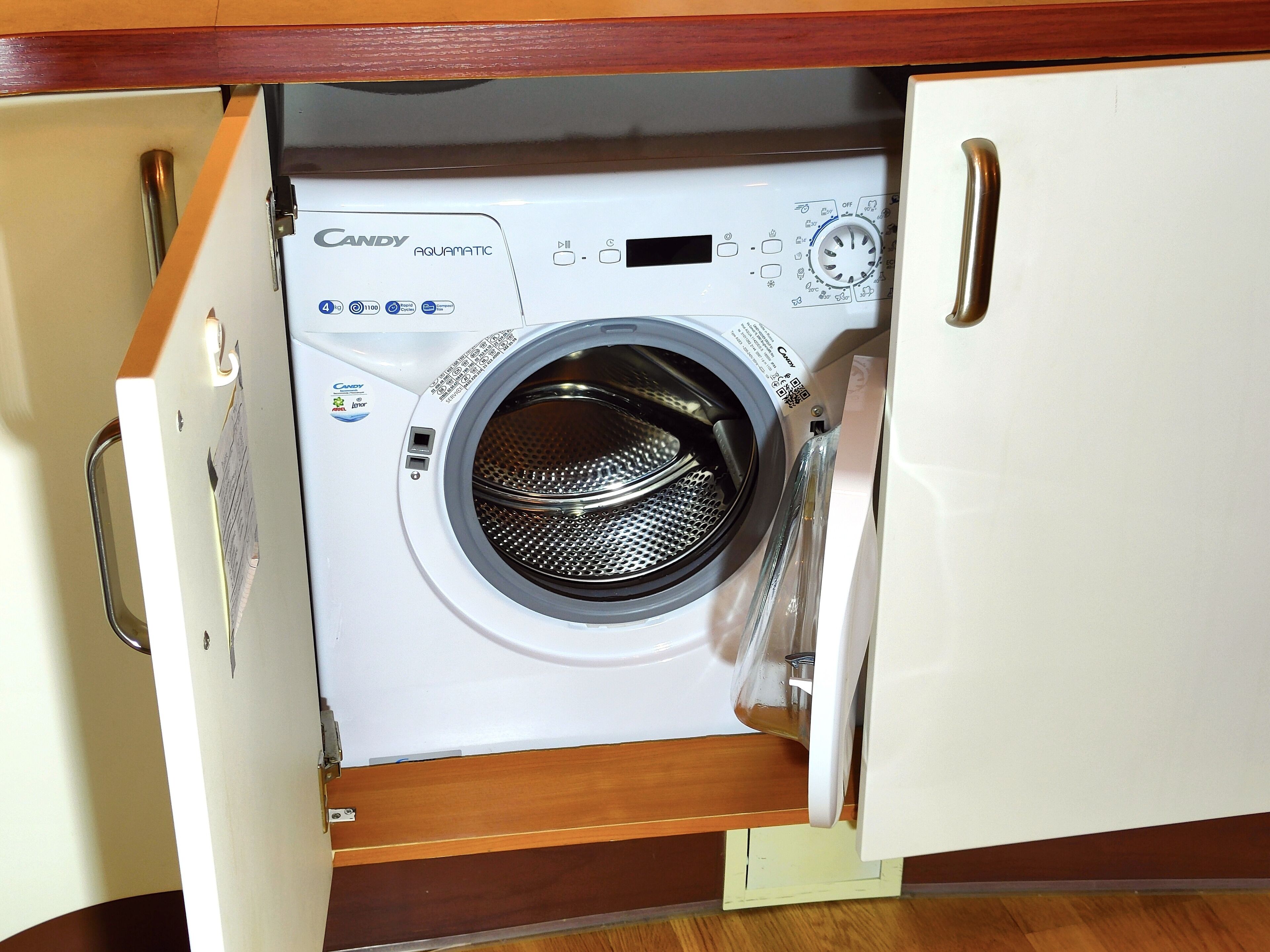 A Candy Aquamatic front-loading washing machine in a wooden cabinet.