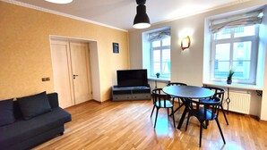 Un salon comprenant un canapé, un téléviseur, une table à manger, des chaises et une plante en pot près de la fenêtre.