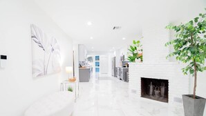 A modern interior with a white fireplace, a large potted plant, and a marble floor. - WPB Elegant 5BR | Hot Tub | Fire Pit | Near Beach (West Palm Beach)