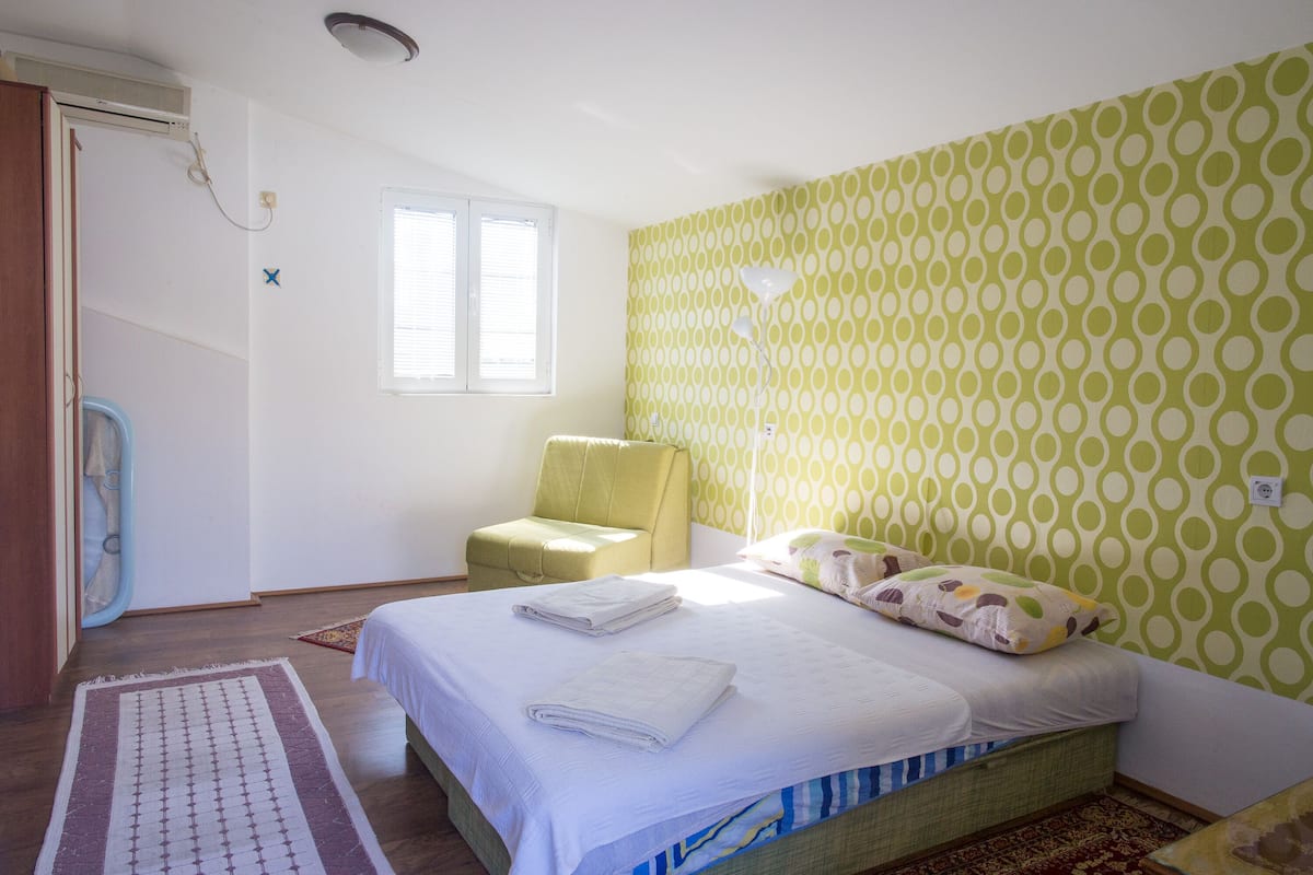 A bedroom with a bed, a chair, a window, and a patterned wall.