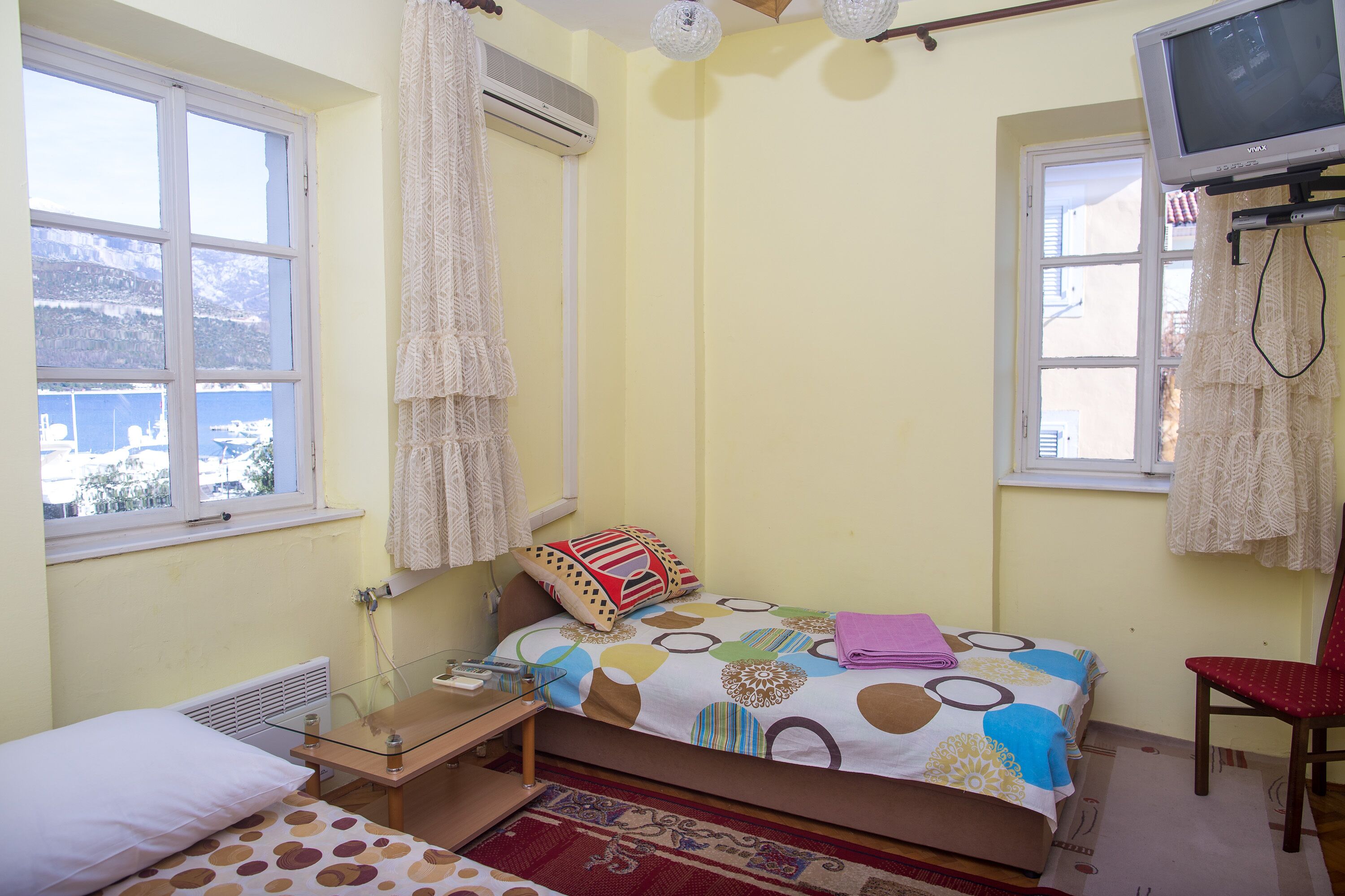 A bedroom with a bed, a chair, a TV, and a window with curtains.