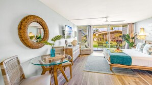 Ein modernes Schlafzimmer mit Glastisch, Korbstühlen, einem Bett mit türkisfarbenem Überwurf und Blick auf einen Garten und ein Haus durch große Schiebetüren.
