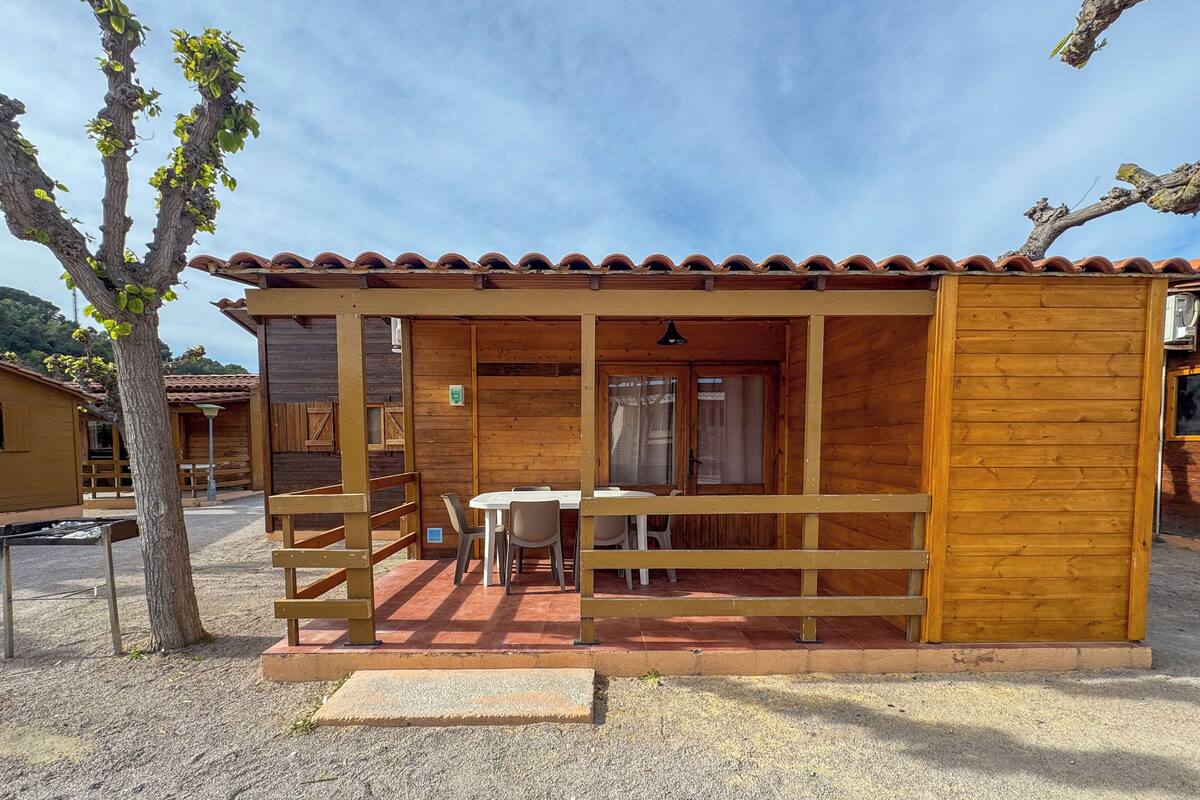 Eine Holzhütte mit Ziegeldach, einer überdachten Veranda mit Tisch und Stühlen sowie einer Treppe, die zu einer oberen Ebene führt.