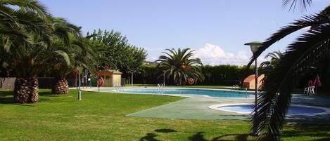 A swimming pool surrounded by palm trees and a small building, likely a poolside bar or lounge area.