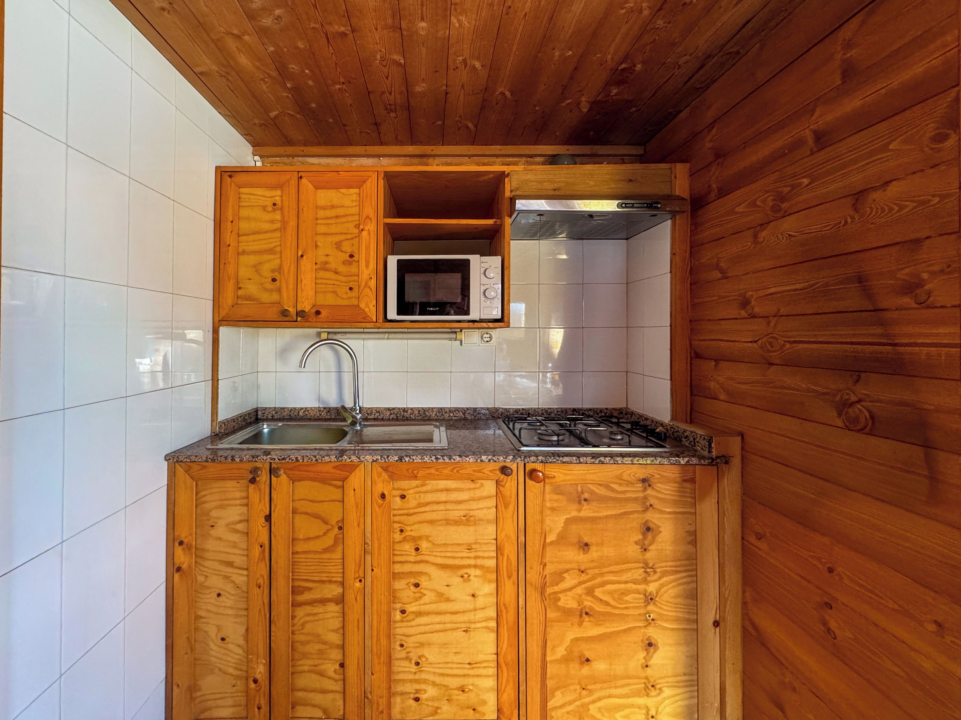 Una cocina compacta con armarios de madera, un lavamanos de acero inoxidable y un microondas.