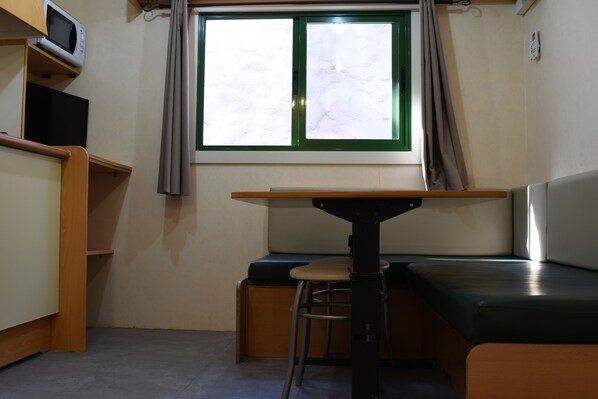 A small room with a table, a bench, a stool, a television, and a window with curtains. - Mediterrani Natura Spa Resort (Tarragona)