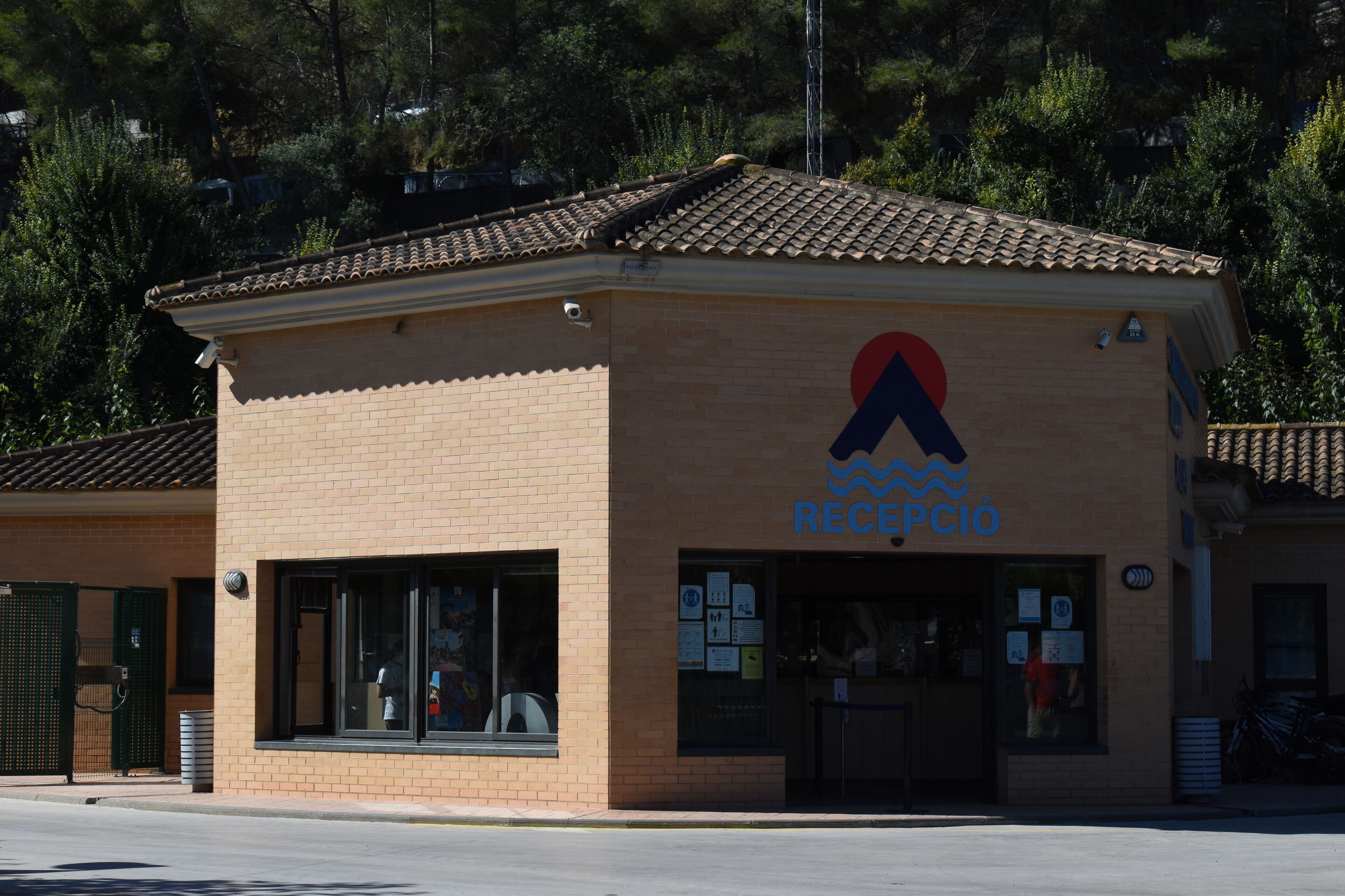 Un pequeño edificio de ladrillo con techo de tejas, un logotipo con una ola azul y un triángulo rojo, y un letrero que dice "RECPCIO".