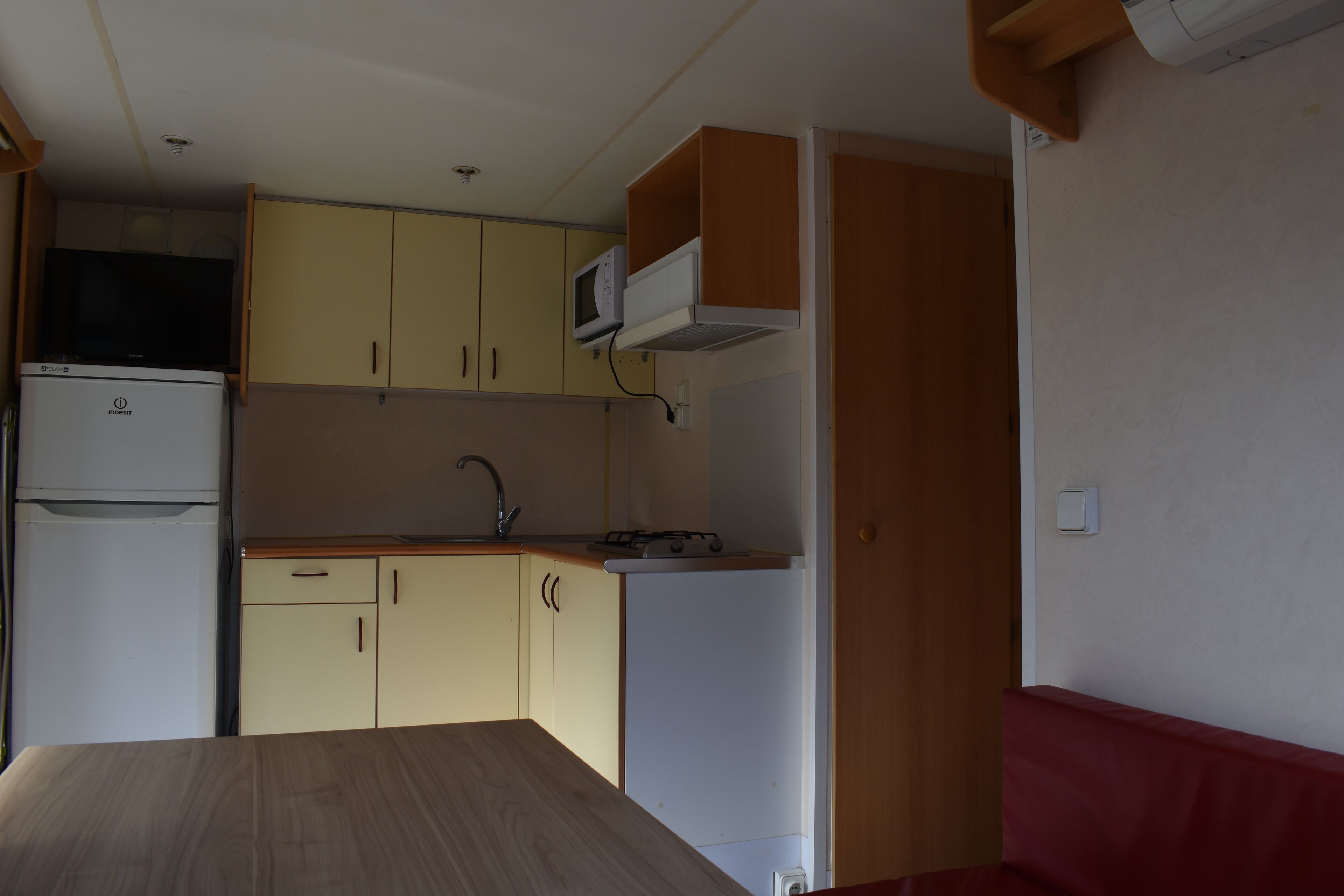 A compact kitchen with a microwave, stove, and sink. There is a small refrigerator and a wooden table.