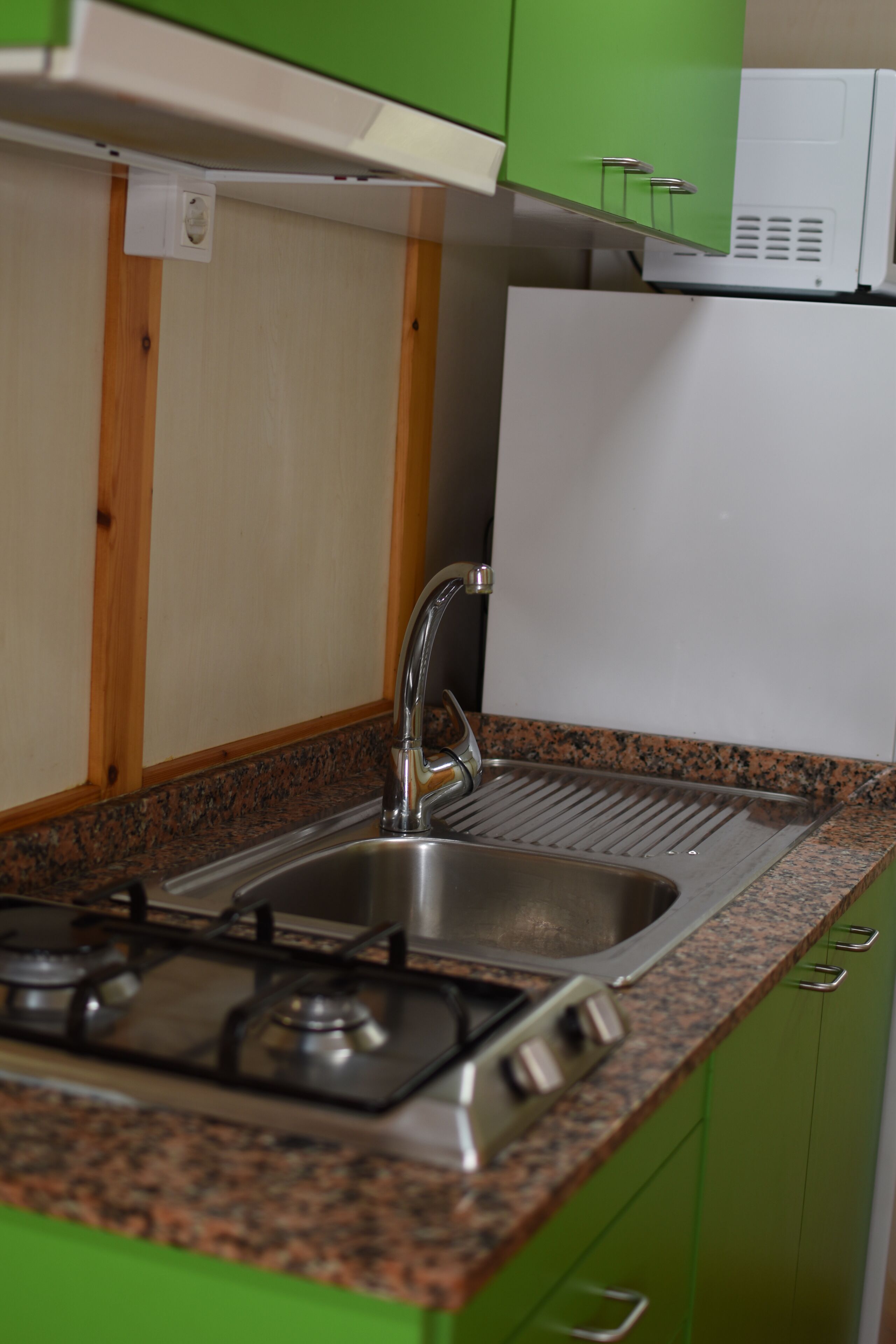 A kitchen with a gas stove, stainless steel sink, and green cabinets.