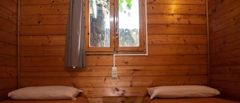 A cabin with two wooden beds, a small table, and a window with a curtain.