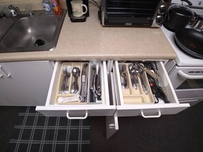 Uma cozinha com uma gaveta contendo utensílios diversos e uma cafeteira sobre a bancada.