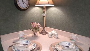 A dining table set with floral tableware, a clock, and a lamp. - All-inclusive Apartment - 1 Bedroom, 1 Bath, Equipped Kitchen, & Laundry (Terre Haute)