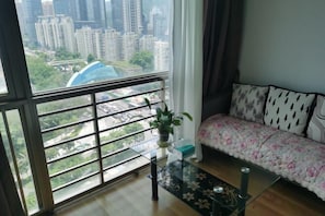A room with a large window, a sofa with patterned cushions, a glass coffee table, and a potted plant. - Shenzhen Four Seasons Family Apartment (Shenzhen)