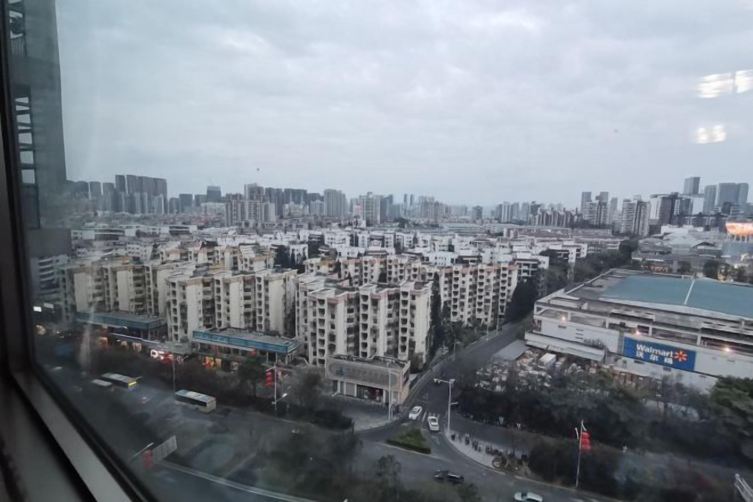 A cityscape view from a window, featuring high-rise buildings, a parking lot, and a road with vehicles.