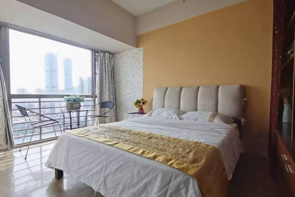 A hotel room with a large bed, a balcony with a chair, and a city view.