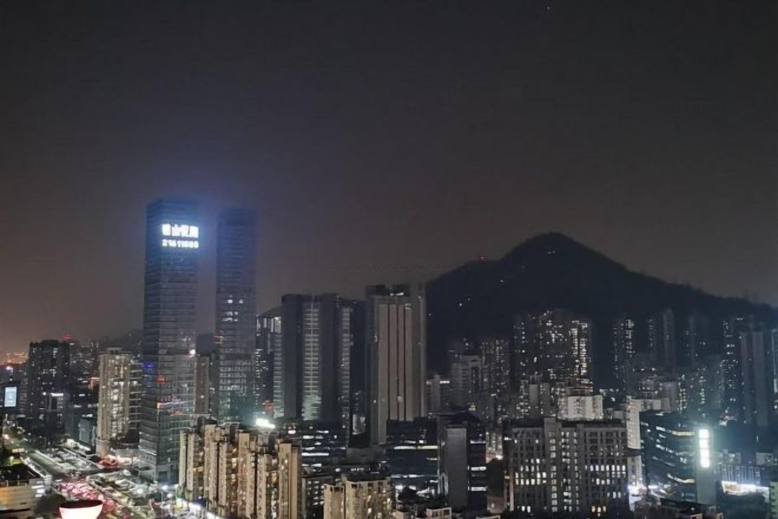 A nighttime cityscape with high-rise buildings and a mountain in the background.