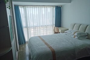 A hotel room with a bed, a chair, a small table, and a window with curtains. - Shenzhen Four Seasons Family Apartment (Shenzhen)