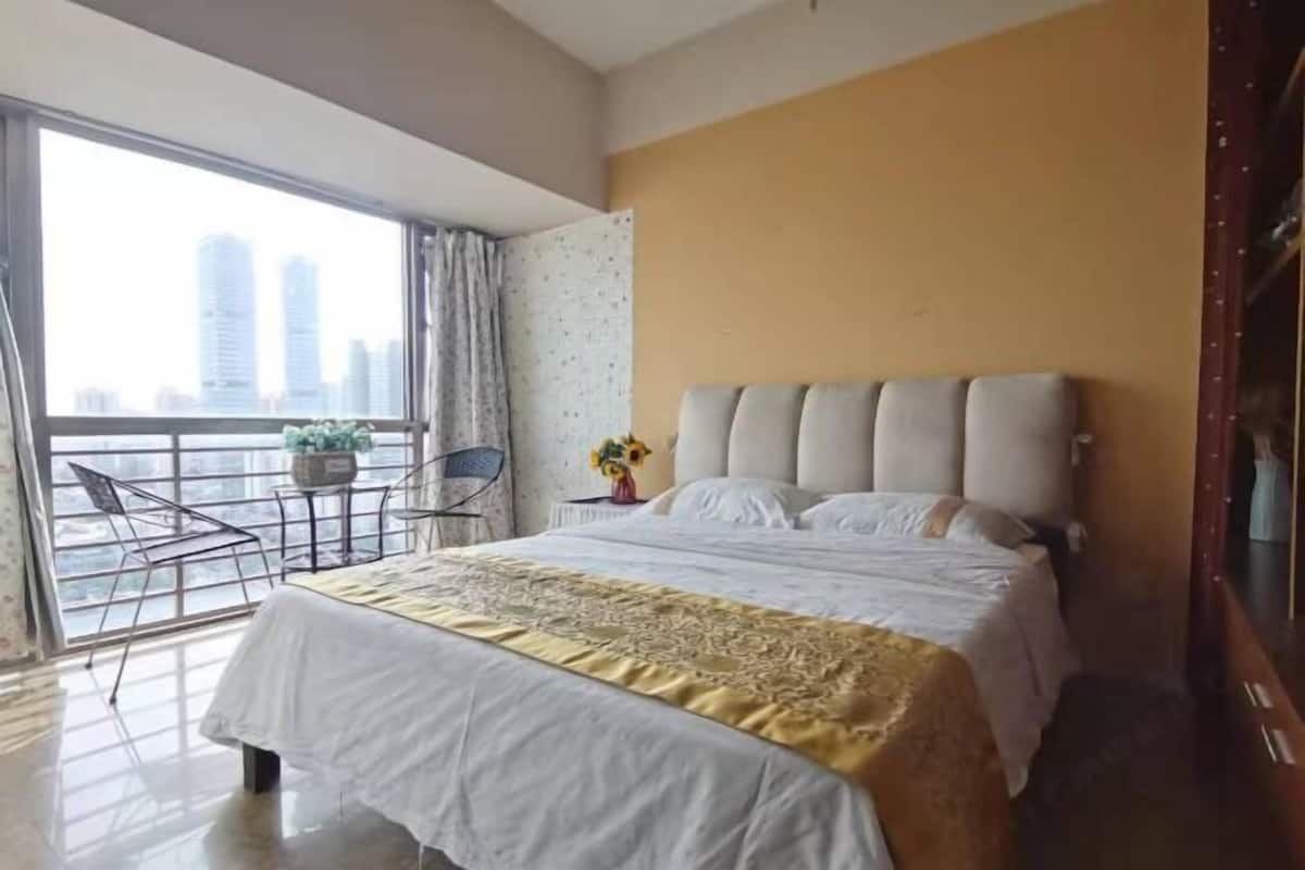A hotel room with a large bed, a balcony with a chair, and a view of tall buildings.