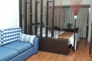 A room with a blue sofa, a dining table with chairs, a small table with a plant, and a partition with curtains. - Shenzhen Four Seasons Family Apartment (Shenzhen)