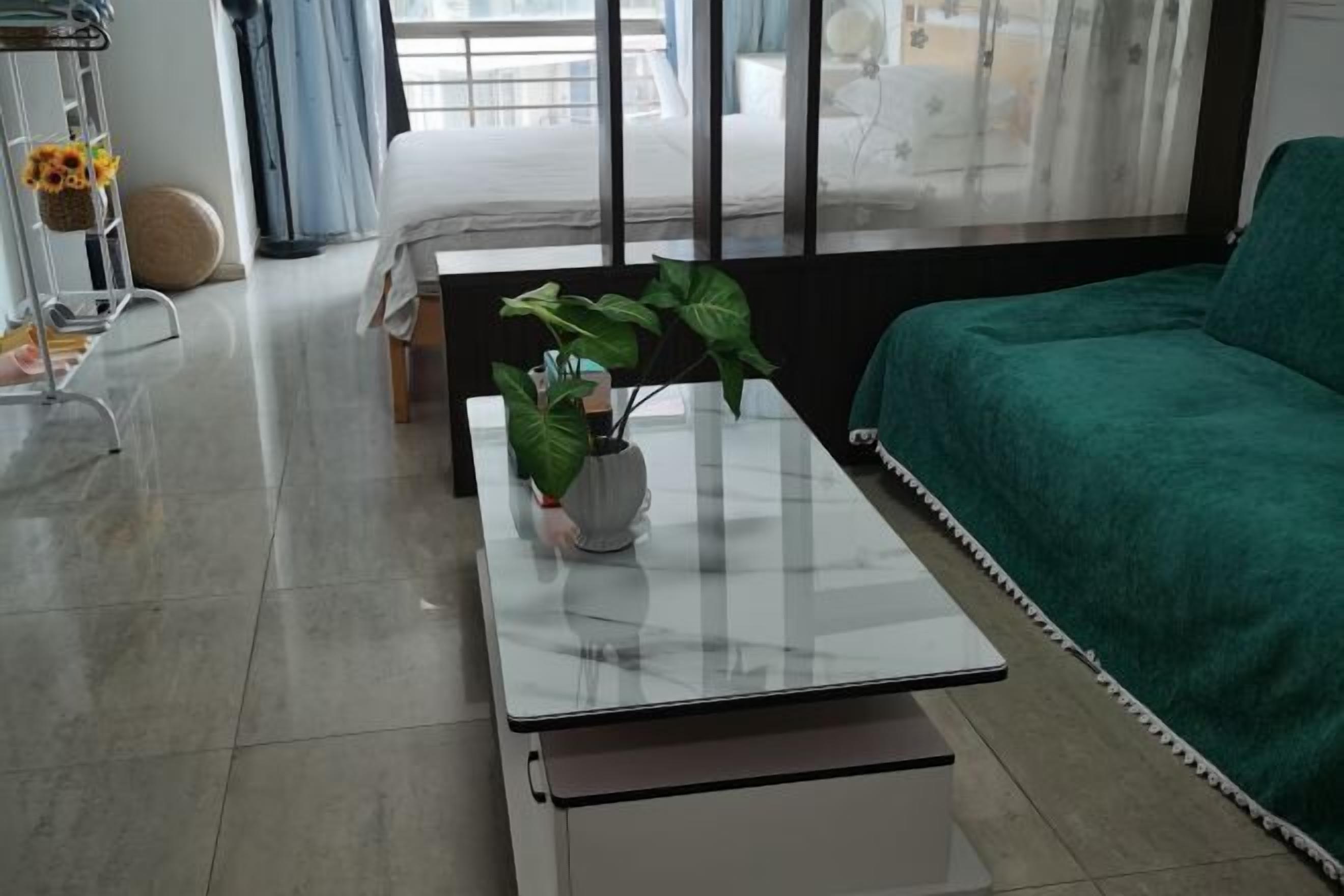 Een moderne woonkamer met een glazen salontafel, een groene bank en een groot raam met gordijnen.