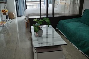 A modern living room with a glass coffee table, a green sofa, and a large window with curtains. - Shenzhen Four Seasons Family Apartment (Shenzhen)