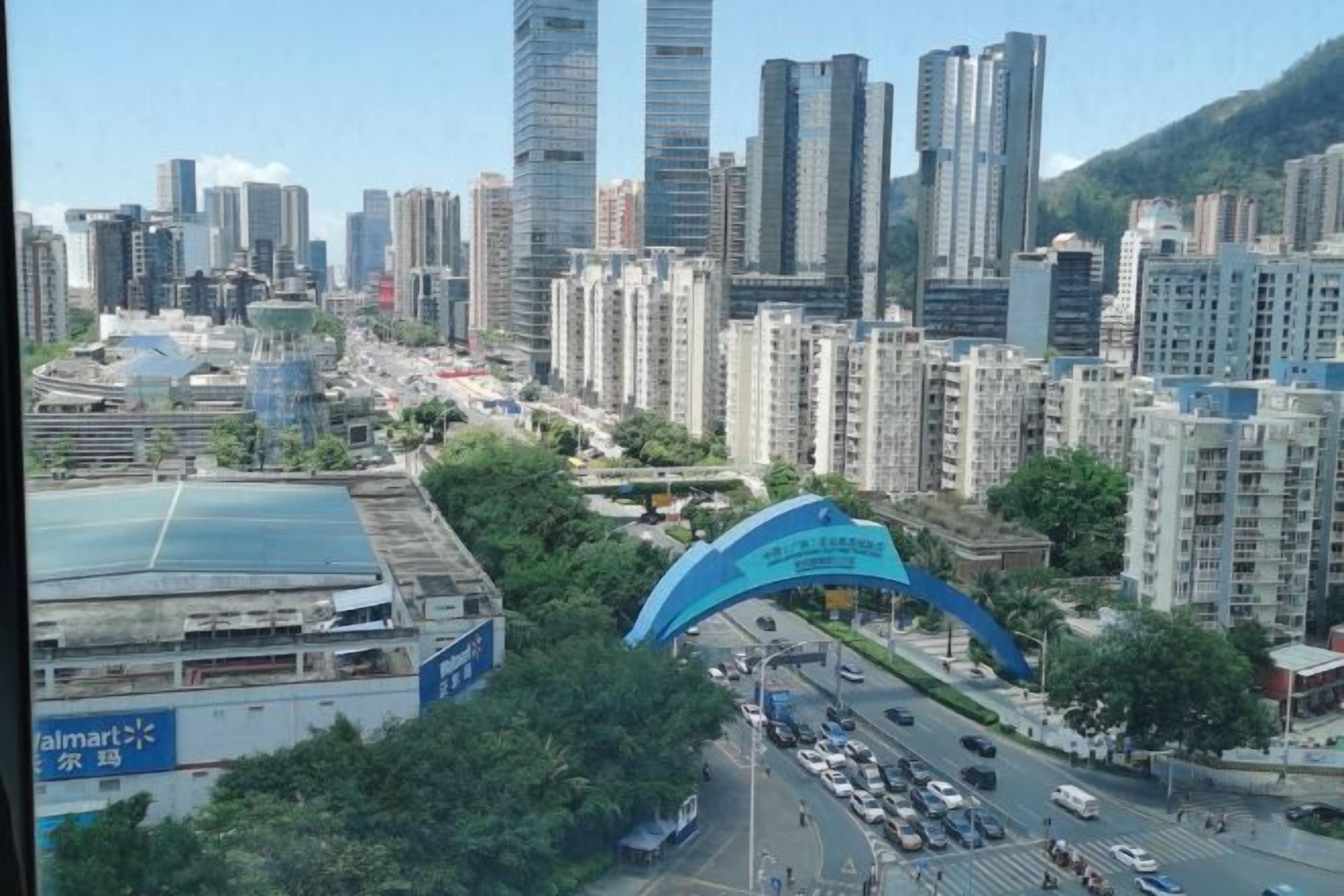 Un paisaje urbano con edificios altos, un gran arco azul y una intersección con mucho tráfico.