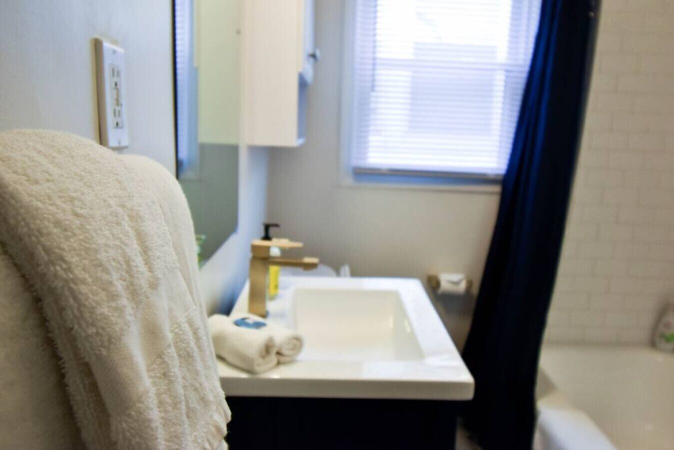 A bathroom with a white sink, a towel, a mirror, and a window with blinds.