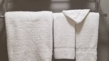 Et badeværelse med toilet, håndklædestang med tre håndklæder og toiletpapirholder.