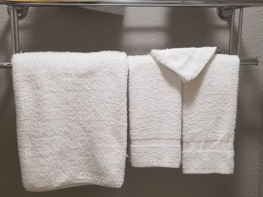 Et badeværelse med toilet, håndklædestang med tre håndklæder og toiletpapirholder.
